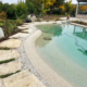 Bio.design-Pool in organisch harmonischer Form mit Randbepflanzung und Terrassenanschluss